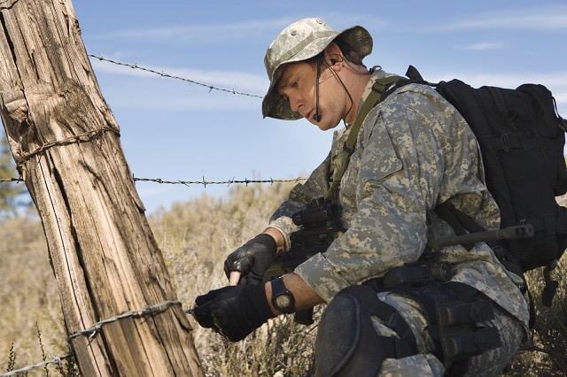 U.S. military soldier working with barbed wire while carrying bag of gear