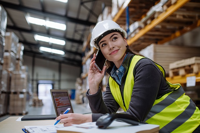 Warehouse manager on the phone working with laptop and warehouse management planning documents