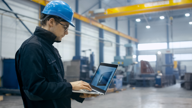 Worker using CMMS software on a laptop in a facility